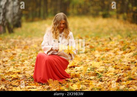 Schöne junge Frau im roten Rock hält Blätter im gelben Herbstpark Stockfoto