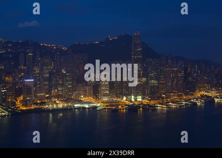 Wolkenkratzer mit heller Beleuchtung, Uferfront und Berge in Hongkong, China bei dunkler Nacht, Blick vom New World Center Stockfoto