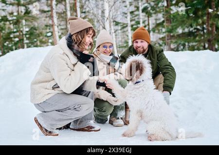 Kaukasischer Mann, Frau und ihre Tochter verbringen den Wintertag im Waldpark, sitzen auf Hunkern und haben Spaß mit ihrem Hund Stockfoto