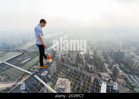 Dachdecker steht auf dem Dach eines Wolkenkratzers inmitten von Nebel, Guangzhou, China Stockfoto