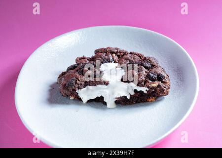 Ein großer, frisch zubereiteter, warmer Oreo-Cookie im NY-Stil, halbiert und auf einem Teller serviert. Der Keks ist mit einer weißen Schokoladencreme gefüllt Stockfoto