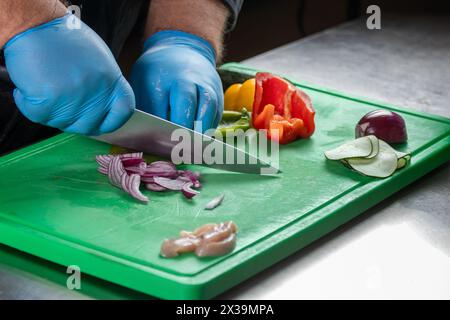 Ein erfahrener Koch bereitet sorgfältig frische Zutaten zu, darunter Fleisch, Zwiebeln, Paprika und Gurken. für ein schmackhaftes Rezept, das kulinarische Ex präsentiert Stockfoto