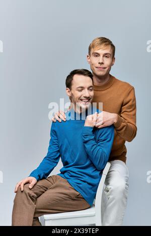 Ein liebevolles schwules Paar in lässiger Kleidung posiert vor grauem Hintergrund. Stockfoto