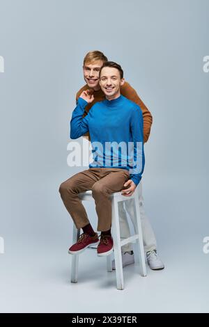 Zwei Männer in lässiger Kleidung, die vor grauem Hintergrund posieren. Stockfoto