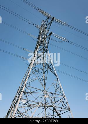 Strompylon und Stromleitungen von unten vor blauem Himmel Stockfoto