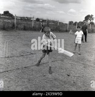 1960er Jahre, historisch, draußen auf einem Feld, ein kleiner Junge, der Cricket spielt, Konzentration und Anstrengung, als vor den Stümpfen, schlägt er Schläger auf den Ball, England, Großbritannien. Stockfoto