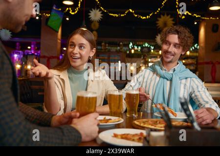 Junge Freunde essen Pizza und trinken Bier, während sie sich im Pub ausruhen Stockfoto