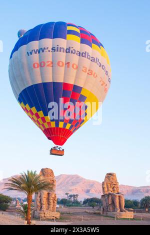 Farbenfrohe Heißluftballons fliegen über die Memnonkolosse bei Sonnenaufgang am Westufer von Luxor, Ägypten Stockfoto