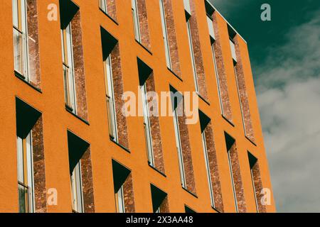 Fragment einer orangen Hausfassade mit langen schmalen Fenstern. Hochhaus-Apartment oder Bürogebäude außen. Abstrakte architektonische gelbe Wand. Stockfoto