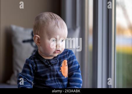 6 Monate alter Junge, der aus dem Fenster blickt. Stockfoto