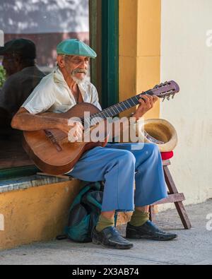 Ein älterer Mann saß auf einer Fensterbank vor einem Geschäft und spielte eine Gitarre für Touristen, um in der Altstadt von Havanna, Kuba, zu betteln. Stockfoto