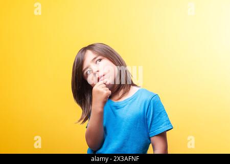 Ein Junge mit braunen Haaren ist nachdenklich mit der Hand am Kinn und trägt ein blaues Hemd. Vorstellung von Reflexion, Meditation, Denken. Kopie sp Stockfoto