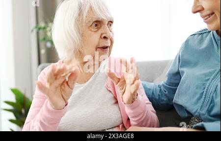 Die alte Großmutter plaudert mit ihrer Enkelin auf Einer kleinen Couch im Flur und erzählt ihr Eine Geschichte aus ihrem langen Leben Stockfoto