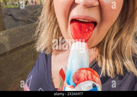 Nahaufnahme einer Frau, die ein rotes, weißes und blaues Eis genießt, mit Fokus auf die Zunge, die vom Leckerli rot gefärbt ist. USA. Stockfoto