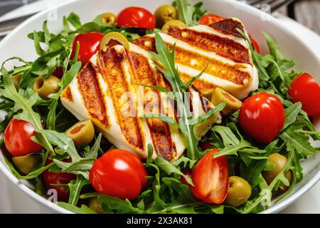 Nahaufnahme mit frischem Salat mit gegrilltem griechischen halloumi-Käse, Raketensalat, Tomaten und grünen Oliven in einer weißen Schüssel Stockfoto