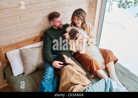 Blick aus dem Hochwinkel, moderne Familie mit Hund, die den Wintertag zu Hause verbringen und sich im Schlafzimmer in einem Holzhaus entspannen Stockfoto