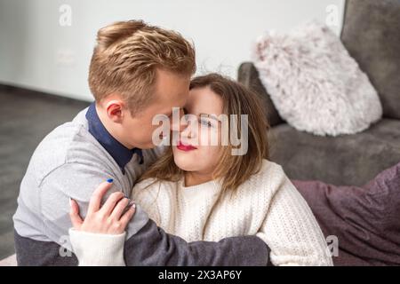Ein Mann küsst liebevoll eine Wange einer Frau, ihre gemütliche Umarmung zeigt Liebe und Behaglichkeit, ein berührender Valentinstag-Moment für ein Paar. Hoher ph-Wert Stockfoto