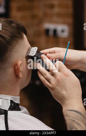 Der Friseur verwendet Haarschneider an der Stirn, am Ohr, am Kinn, am Tempel Stockfoto