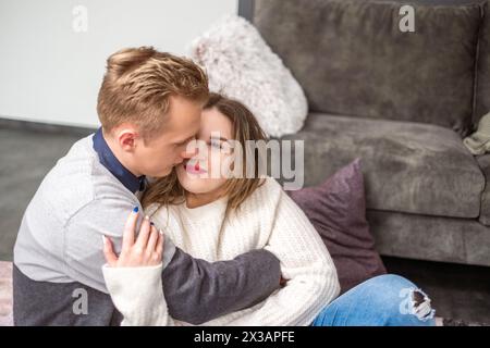 Ein Mann küsst liebevoll eine Wange einer Frau, ihre gemütliche Umarmung zeigt Liebe und Behaglichkeit, ein berührender Valentinstag-Moment für ein Paar. Hochwertige Pho Stockfoto