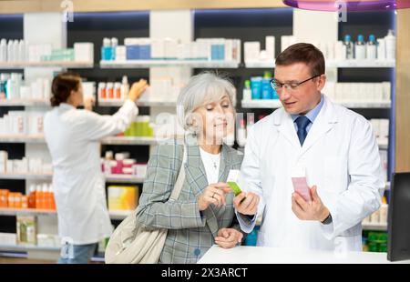 Pharmazeutischer Mann mittleren Alters, der alte Kundschaft über Pflegemittel in Box berät Stockfoto