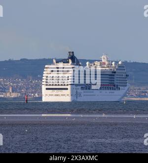 Belfast Lough, County Down, Nordirland, Großbritannien. April 2024. UK Wetter - ein sonniger Abend auf Belfast Lough, aber immer noch kalt im Wind. Das Kreuzfahrtschiff MSC Poesia am Belfast Lough verlässt den Hafen von Belfast mit der mittelalterlichen normannischen Burg Carrickfergus auf der linken Seite. Quelle: CAZIMB/Alamy Live News. Stockfoto