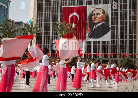 Izmir, Türkei - 23. April 2024: Fröhlicher Tanz von Kindern in Rot und weiß, mit türkischen Fahnen und Atatürks Porträt im Hintergrund während Nat Stockfoto