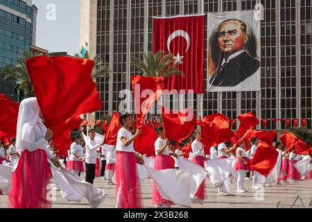 Izmir, Türkei - 23. April 2024: Fröhlicher Tanz von Kindern in Rot und weiß, mit türkischen Fahnen und Atatürks Porträt im Hintergrund während Nat Stockfoto