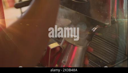 Bild: Hände eines Barista, der Milch aufschäumt, indem er die Maschine in einem Café verwendet Stockfoto