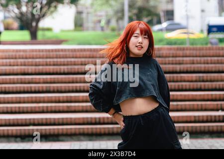 Koreanische Frau mit rotem Haar, die auf den Stufen der Stadt eine Tanzposition anschlägt. Stockfoto