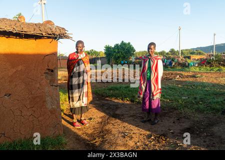 Februar 2024. Masai Mara Nationalpark. Maasai-Frauen stehen in der Nähe von Lehmhütten. Traditionelles Leben in einem Maasai-Dorf in Ostafrika. Stockfoto