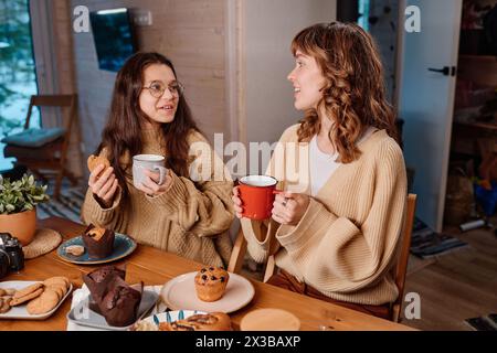 Blick aus einem hohen Winkel auf Mutter und Tochter, die Tassen halten, Desserts essen, Tee trinken und sich während des Familienessens unterhalten Stockfoto