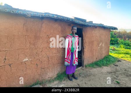 Februar 2024. Masai Mara Nationalpark. Maasai-Frauen stehen in der Nähe von Lehmhütten. Traditionelles Leben in einem Maasai-Dorf in Ostafrika. Stockfoto