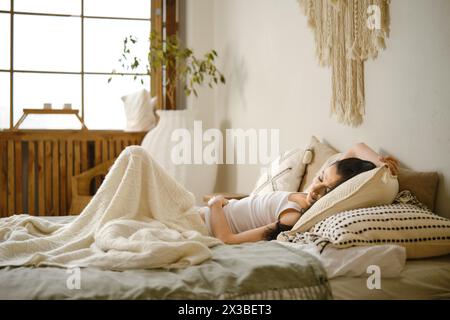 Friedliche Frau im Schlafanzug, die schlafend in einem gemütlichen Bett auf weichen Kissen schläft Stockfoto