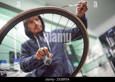 Hispanischer Mann, der an einem Fahrradgemälde arbeitet. Zeit zum Entfernen des Abdeckbands der Radfelge. Nahaufnahme der Hände. Stockfoto