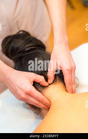 Vertikale Nahaufnahme und Draufsicht eines professionellen Masseurs, der einer entspannten Frau eine Nackenmassage gibt Stockfoto