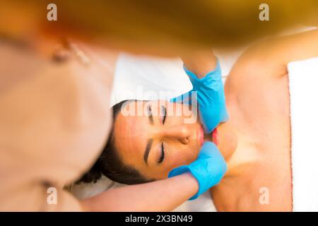Draufsicht einer kaukasischen erwachsenen Frau, die auf einer Liege liegt und eine Kiefermassage erhält, um Spannungen zu lösen Stockfoto
