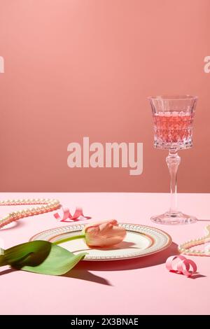 Eine Blume liegt auf einem Teller, umgeben von Perlenketten und rosafarbenen Papierfeuerwerken. Ein Glas gefüllt mit rosa Wein. Partykonzept Stockfoto