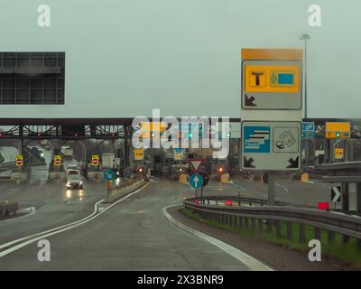 Autos nähern sich Mautstellen auf einer nassen Straße mit Verkehrsschildern über der Autobahn A1 A8 in der Nähe von Mailand, Italien Stockfoto