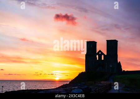 Sonnenuntergang über dem Meer an den Ruinen der Doppeltürme der angelsächsischen Kirche in Reculver an der Küste von Kent in der Nähe der Herne Bay. Die Türme haben fast eine Silhouette vor einem leuchtend gelben und rotrosa Himmel. Stockfoto