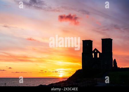 Sonnenuntergang über dem Meer an den Ruinen der Doppeltürme der angelsächsischen Kirche in Reculver an der Küste von Kent in der Nähe der Herne Bay. Die Türme haben fast eine Silhouette vor einem leuchtend gelben und rotrosa Himmel. Stockfoto