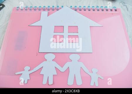 Haus aus Papierkram mit Familienfiguren auf hölzernem Hintergrund Metapher für den Traum vom Hausbesitz Stockfoto