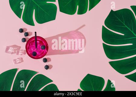 Sommerszene mit kaltem rosa erfrischendem Getränk und tropischen grünen Blättern auf rosa Hintergrund. Sonne und Schatten. Minimales Cocktailkonzept. Stockfoto