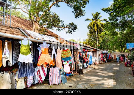 Cochin, Indien - 22. März 2024: Menschen verkaufen farbenfrohe Kleidung an Touristen, umgeben von großen Palmen. Stockfoto