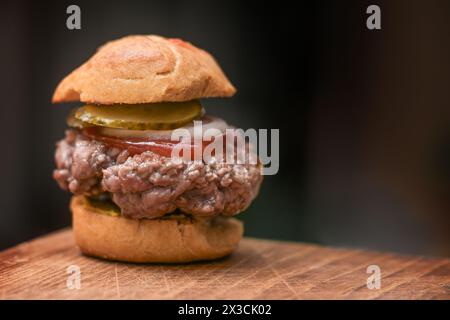 Mini-Burger mit Brötchen, Senf, Rindfleisch, Ketchup, Zwiebeln und Gurke auf rustikalem Holzbrett vor dunklem Hintergrund, Kopierraum, ausgewählt Stockfoto