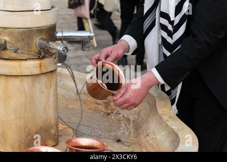 Nahaufnahme eines Mannes, der eine kupferne Natla oder einen jüdischen rituellen Handwaschbecher benutzt, um seine Hände rituell zu waschen, bevor er an der Westmauer in Jerusalem, ISR, betet Stockfoto