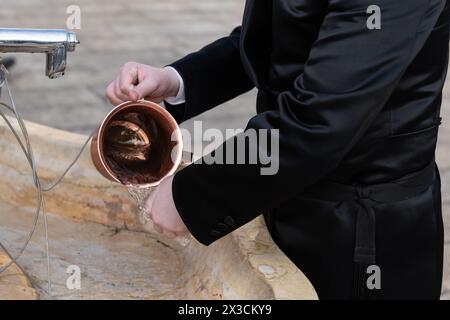 Nahaufnahme eines Mannes, der eine kupferne Natla oder einen jüdischen rituellen Handwaschbecher benutzt, um seine Hände rituell zu waschen, bevor er an der Westmauer in Jerusalem, ISR, betet Stockfoto