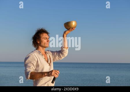 Aufmerksamer Mann, der mit tibetischer Klangschale auf dem Meer meditiert Stockfoto