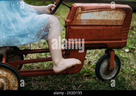 Kind, das auf dem Hof auf einem alten Trettraktor reitet Stockfoto