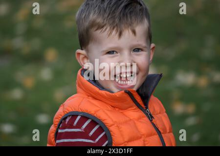 Fröhlicher Junge in orangefarbener Weste, der im Herbst draußen lacht Stockfoto