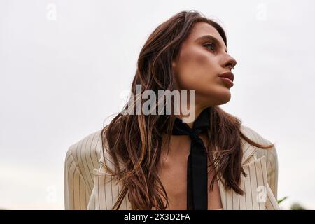 Eine auffällige Frau mit fließenden langen Haaren, elegant mit einer schwarzen Krawatte verziert, die in einer natürlichen Umgebung Ausstrahlung und Eleganz ausstrahlt. Stockfoto